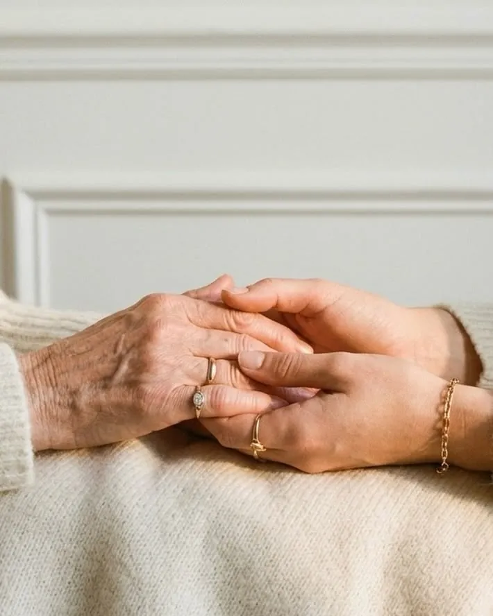 Mano giovane che stringe la mano di una persona anziana, appoggiate su un plaid di lana chiara
